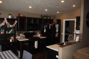 Kitchen featuring recessed lighting, light countertops, black appliances, and dark cabinetry