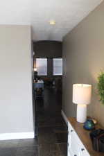 Hall featuring stone finish flooring, baseboards, and a textured ceiling