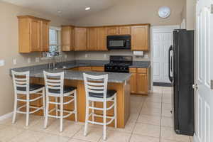 Kitchen featuring light tile patterned floors, a kitchen breakfast bar, vaulted ceiling, black appliances, and a sink