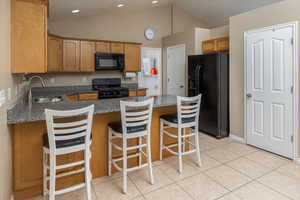 Kitchen featuring a breakfast bar area, light tile patterned flooring, a sink, black appliances, and dark stone countertops