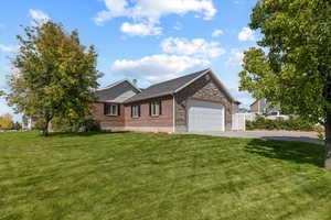 View of front of property with driveway, a garage, stone siding, a front lawn, and brick siding