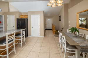 Kitchen featuring light tile patterned floors, black refrigerator with ice dispenser, lofted ceiling, and a notable chandelier