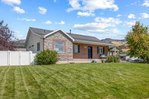 View of front of house featuring a front yard, stone siding, fence, and a gate