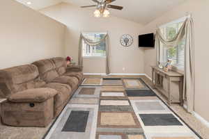 Living room featuring carpet, baseboards, vaulted ceiling, and a ceiling fan