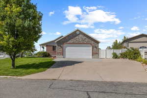 Ranch-style home with an attached garage, a front yard, fence, stone siding, and driveway