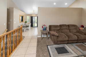 Living room featuring light tile patterned floors, baseboards, lofted ceiling, a notable chandelier, and recessed lighting