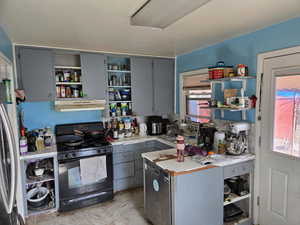 Kitchen featuring black gas range, under cabinet range hood, light countertops, freestanding refrigerator, and open shelves