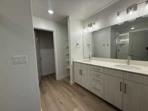 Full bath with double vanity, a textured ceiling, a sink, and wood finished floors