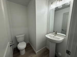 Half bathroom with toilet, a sink, baseboards, and wood finished floors