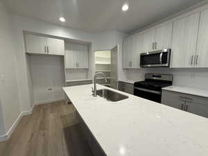 Kitchen with light stone counters, wood finished floors, a sink, appliances with stainless steel finishes, and backsplash