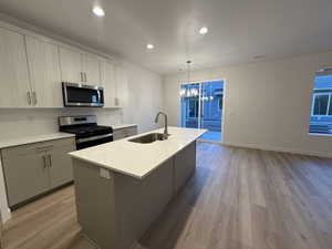 Kitchen featuring stainless steel appliances, a sink, light wood-style floors, an island with sink, and pendant lighting