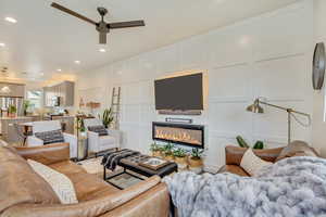 Living area featuring recessed lighting, a decorative wall, a ceiling fan, and a glass covered fireplace