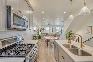 Kitchen featuring appliances with stainless steel finishes, open floor plan, light stone countertops, gray cabinetry, white tiled backsplash, and a stainless steel sink