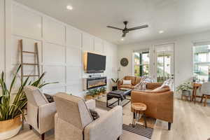 Living room with recessed lighting, a decorative wall, a ceiling fan, a glass covered fireplace, and light wood-type flooring