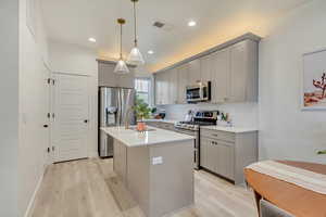Kitchen featuring decorative light fixtures, light countertops, appliances with stainless steel finishes, and a center island with stainless steel sink