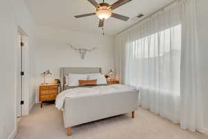 Bedroom with a ceiling fan, light colored carpet, and windows with unobstructed views