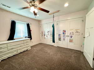 Unfurnished bedroom with dark colored carpet, visible vents, ceiling fan, and two closets