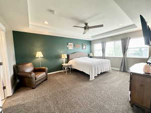 Carpeted bedroom featuring baseboards, a raised ceiling, and a textured ceiling