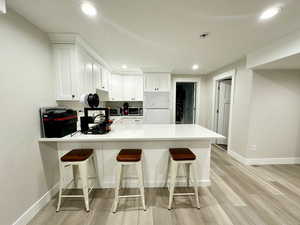 Kitchen with a breakfast bar, white cabinetry, light countertops, freestanding refrigerator, and stainless steel microwave