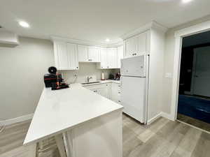 Kitchen with a peninsula, a sink, white cabinets, light countertops, and freestanding refrigerator