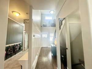 Hall with stairs, plenty of natural light, wood finished floors, and a towering ceiling