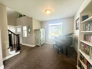 Sitting room featuring a textured ceiling, stairway, dark carpet, and baseboards