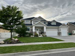 Craftsman-style house featuring concrete driveway, stone siding, a gate, fence, and board and batten siding