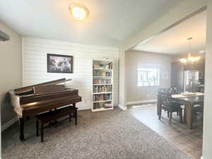 Sitting room featuring a textured ceiling, a notable chandelier, wood walls, wood finished floors, and baseboards