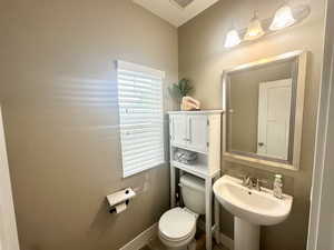 Half bath with baseboards, a sink, visible vents, and toilet