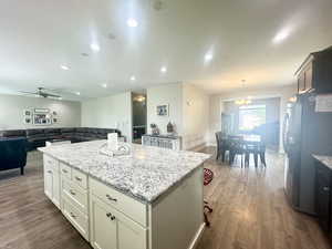 Kitchen featuring dark wood finished floors, light stone counters, open floor plan, decorative light fixtures, and freestanding refrigerator