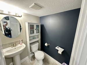 Half bathroom with a textured ceiling, tile patterned flooring, toilet, visible vents, and baseboards