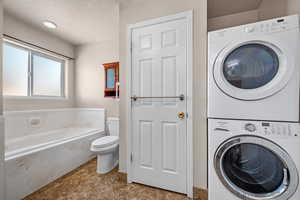 Laundry room featuring a textured ceiling, laundry area, and stacked washing maching and dryer