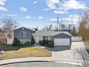 Split level home with brick siding, driveway, an attached garage, and fence