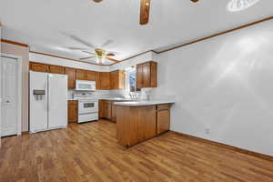 Kitchen featuring light countertops, brown cabinetry, a ceiling fan, white appliances, and a peninsula