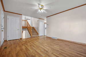 Spare room with a ceiling fan, visible vents, stairs, light wood finished floors, and crown molding