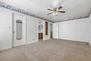 Unfurnished bedroom with a ceiling fan, visible vents, connected bathroom, and light colored carpet