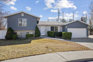 Tri-level home with brick siding, an attached garage, a front yard, fence, and driveway