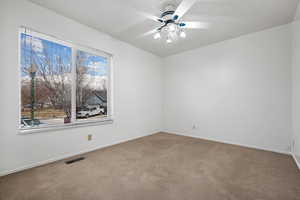 Carpeted empty room featuring a ceiling fan, visible vents, and baseboards