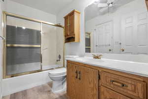 Bathroom featuring enclosed tub / shower combo, ceiling fan, toilet, wood finished floors, and vanity