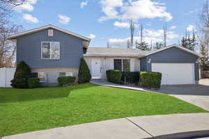 Split level home featuring brick siding, concrete driveway, an attached garage, fence, and a front lawn