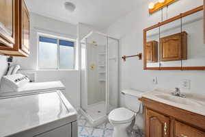 Bathroom with a stall shower, toilet, washer and clothes dryer, and vanity