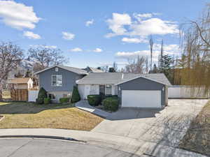 Split level home with a garage, brick siding, fence, concrete driveway, and a front yard