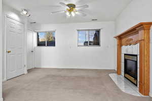 Unfurnished living room featuring a wealth of natural light, visible vents, a tiled fireplace, and light colored carpet