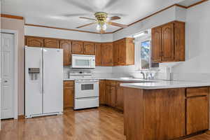 Kitchen featuring light countertops, white appliances, brown cabinetry, and a sink