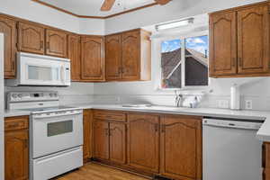 Kitchen with light countertops, white appliances, brown cabinetry, and crown molding