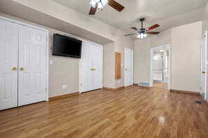 Unfurnished bedroom with light wood-style flooring, visible vents, baseboards, vaulted ceiling, and two closets