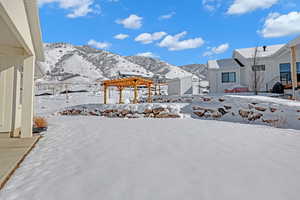 Yard covered in snow featuring a mountain view and a pergola