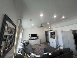 Living area featuring lofted ceiling, recessed lighting, visible vents, a barn door, and ceiling fan