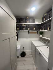 Washroom with a textured ceiling, laundry area, separate washer and dryer, baseboards, and light wood finished floors