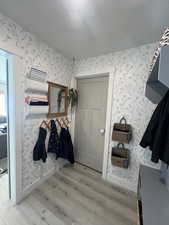 Mudroom featuring a textured ceiling, light wood-style floors, baseboards, and wallpapered walls